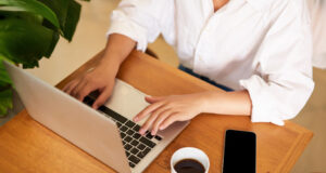 Cropped shot of female hands typing on laptop keyboard, drinking coffee, working in cafe, studying, doing homework